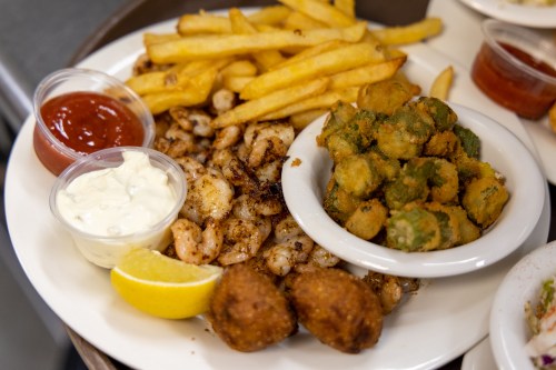 A plate of shrimp with fries, fried okra, and dipping sauces, garnished with lemon wedges.