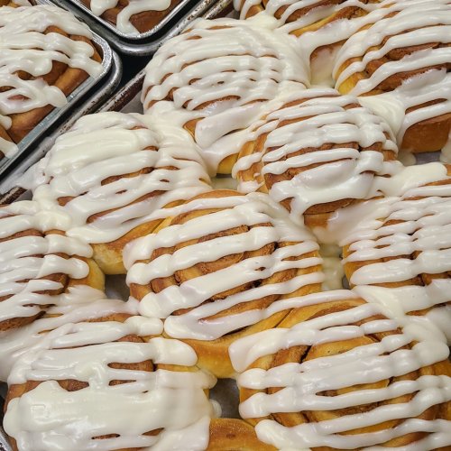 A close-up of freshly baked cinnamon rolls drizzled with white icing, arranged in a tray.
