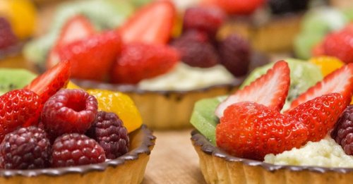 Colorful fruit tarts topped with strawberries, raspberries, kiwi, and mandarin slices on a wooden surface.