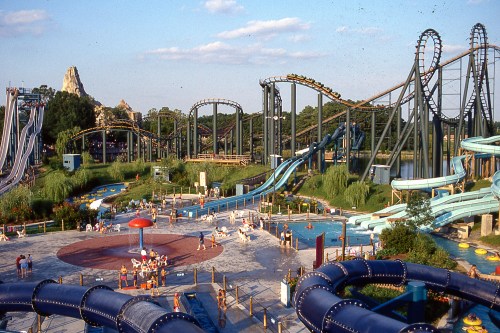 A vibrant amusement park scene featuring roller coasters, water slides, and families enjoying the attractions.