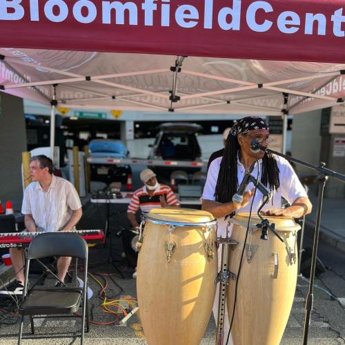 Musicians performing under a tent, with a drummer on congas and a keyboardist in the background.