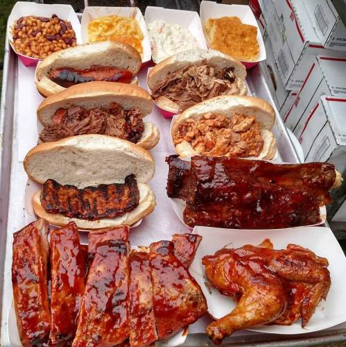 A variety of barbecue dishes including sandwiches, ribs, and chicken, served on a tray with sides.