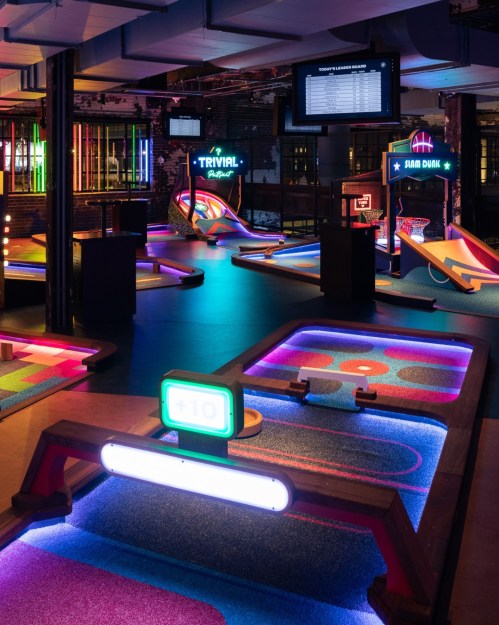 A vibrant indoor mini-golf course with neon lights, colorful obstacles, and a scoreboard in a lively atmosphere.
