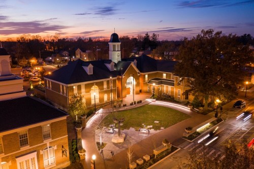 Aerial view of a brick building with a clock tower, surrounded by a landscaped courtyard at sunset.