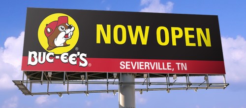 Billboard advertising Buc-ee's, stating "NOW OPEN" in Sevierville, TN, with a bright blue sky in the background.