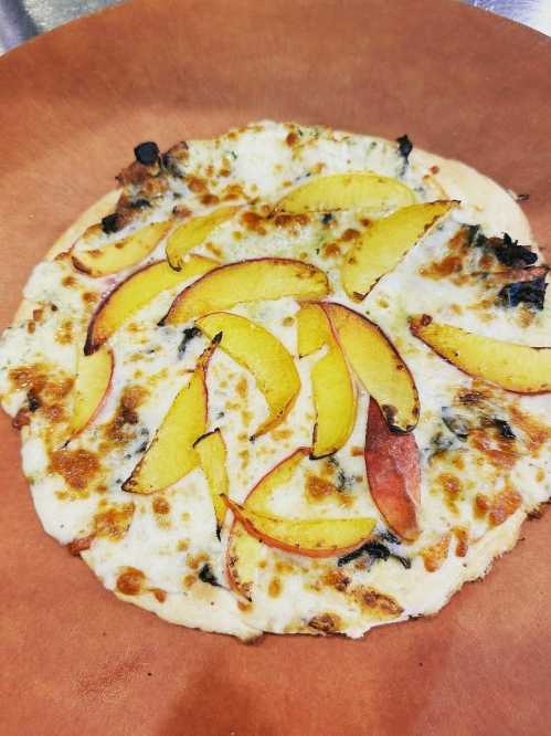 A freshly baked pizza topped with melted cheese and slices of peach on a brown plate.