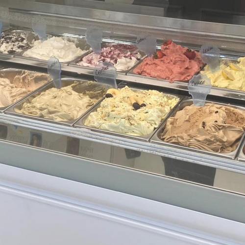 A display of various gelato flavors in metal containers, with labels indicating each flavor.
