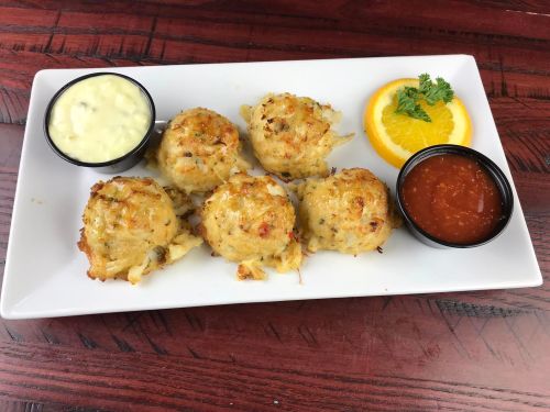A plate of five golden crab cakes served with tartar sauce, cocktail sauce, and a slice of orange for garnish.