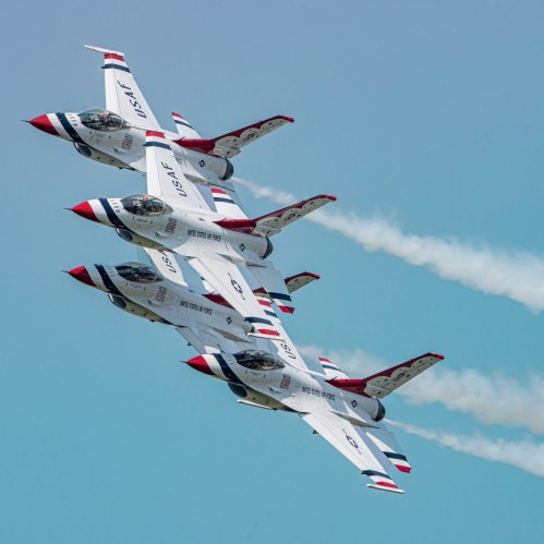 Four military jets flying in a tight formation, leaving trails of smoke against a clear blue sky.