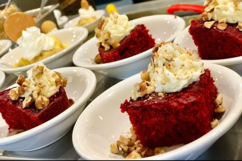 Red velvet cake squares topped with whipped cream and chopped nuts, served in small white bowls.