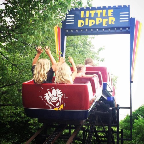 Two children with blonde hair raise their hands in excitement on the "Little Dipper" roller coaster.