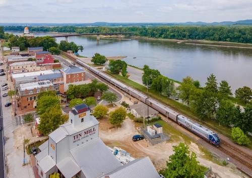 Aerial view of a riverside town with a train passing by, buildings, and lush greenery along the water's edge.
