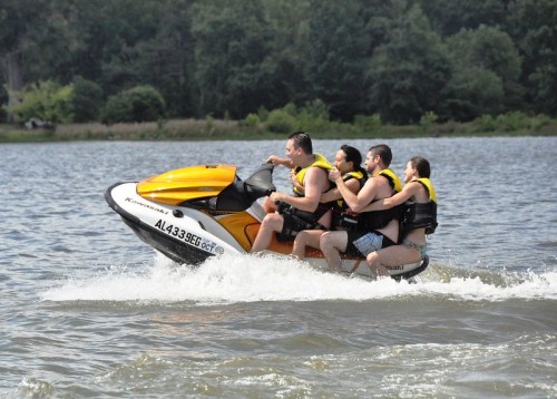 A group of four people enjoying a ride on a yellow jet ski on a lake, wearing life jackets.