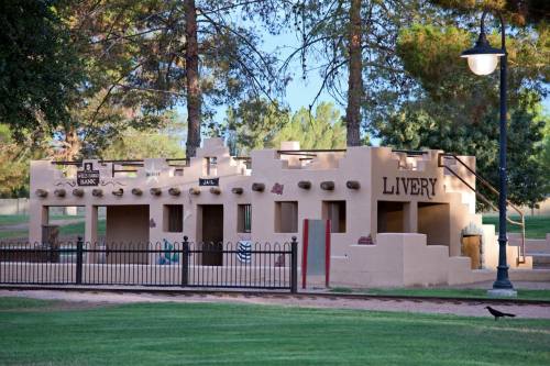 A southwestern-style building with "LIVERY" sign, surrounded by trees and a grassy area, featuring a fence and lamppost.