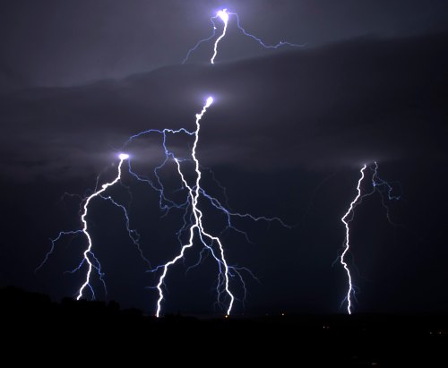Dramatic lightning strikes illuminate a dark, stormy sky, creating a striking contrast against the clouds.