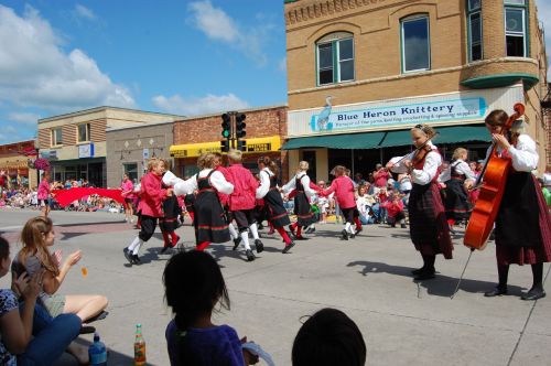 A lively parade scene with dancers in traditional costumes and musicians, while spectators enjoy the festivities.