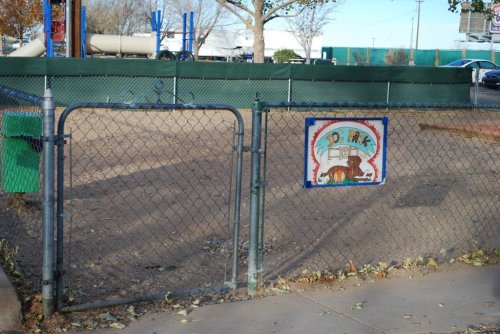 A fenced playground entrance with a sign reading "Joe's Park" and a barren play area in the background.