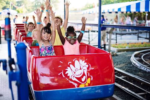 A group of children joyfully raising their hands while riding a colorful amusement park train.