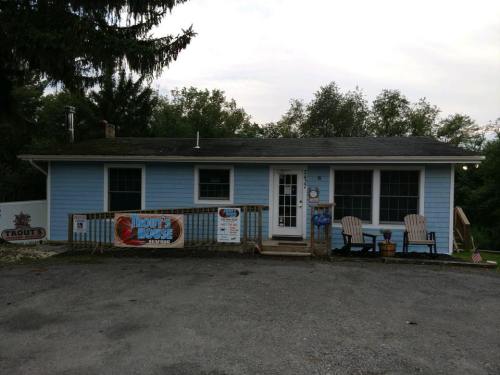 A blue house with a porch and two chairs, featuring a sign that reads "Trout's House" and surrounded by trees.