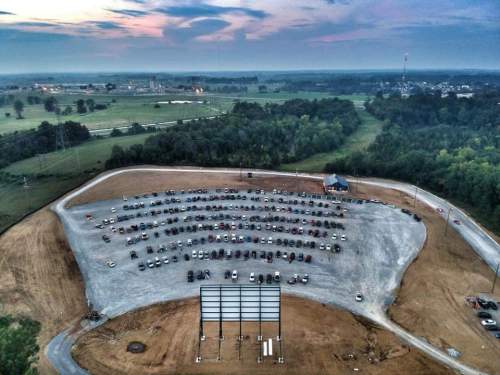 Aerial view of a drive-in movie theater with a large parking area filled with cars and a blank screen at dusk.