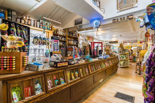 A colorful gift shop interior filled with various souvenirs, snacks, and drinks, featuring a wooden display counter.