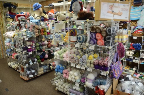 A craft store aisle filled with colorful yarns and knitting supplies displayed on wire shelves.
