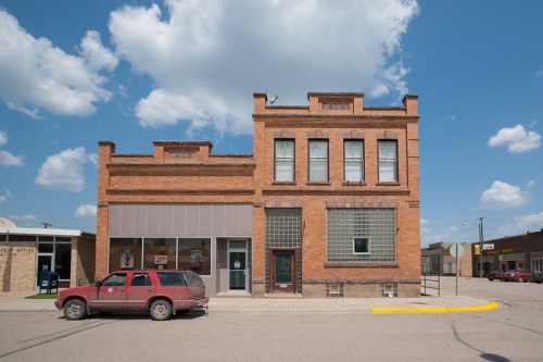 Historic brick building with large windows and a red SUV parked in front, under a blue sky with fluffy clouds.