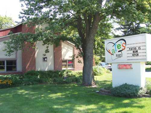 A brick building with a sign reading "Kate's Place" and "Patio is now open," surrounded by greenery.