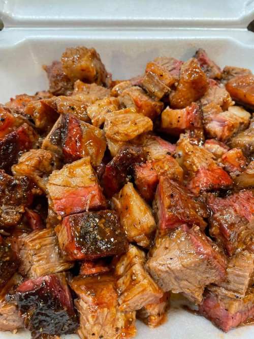 A close-up of diced, smoky barbecue meat with a glossy sauce, served in a white takeout container.