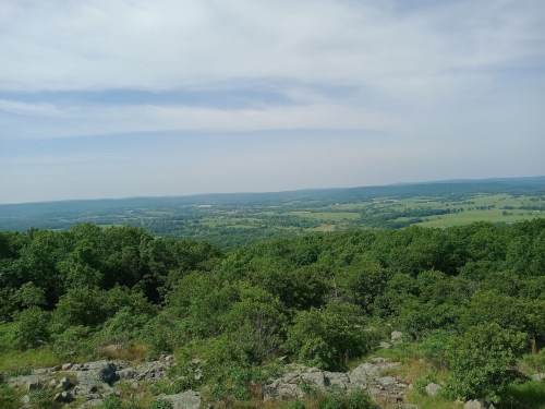 A panoramic view of lush green hills and valleys under a partly cloudy sky.