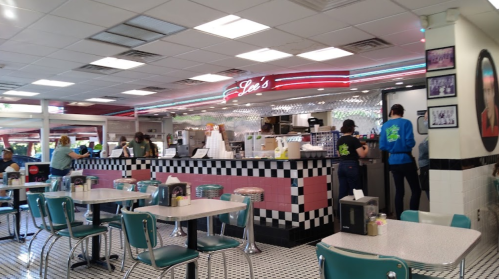A retro diner interior with a checkered floor, colorful seating, and a bustling counter area.