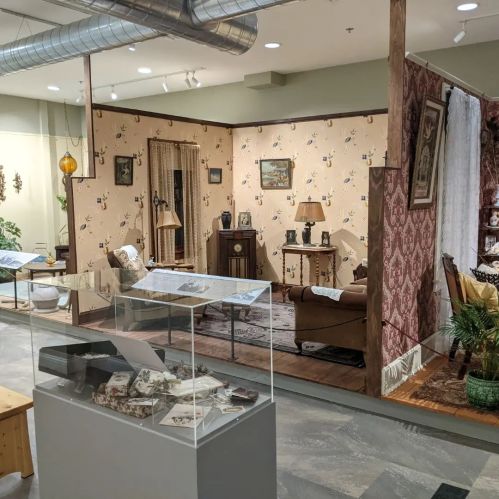 A vintage-style room display featuring patterned wallpaper, furniture, and decorative items in a museum setting.