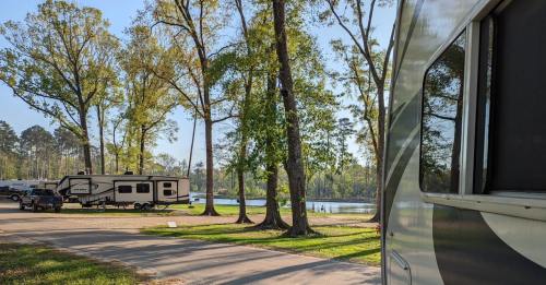 A serene campsite by a lake, featuring RVs, trees, and people enjoying the outdoors on a sunny day.