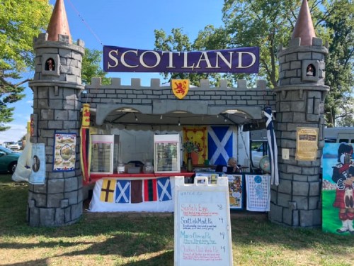 A festive booth themed like a castle, featuring Scottish flags and a menu with traditional items for sale.