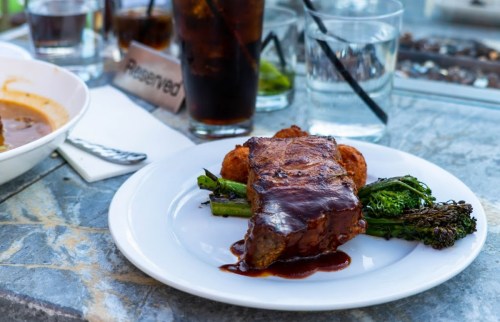 A plate with glazed meat, asparagus, and crispy sides, accompanied by drinks on a table.