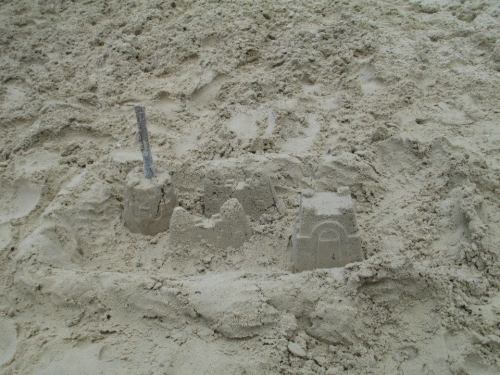 A small sandcastle with towers and a flag, surrounded by smooth sand on a beach.