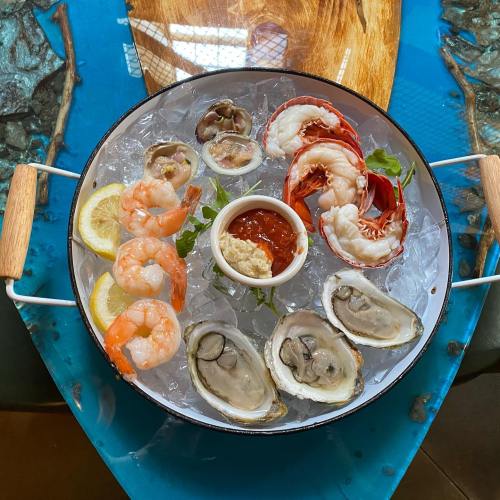 A seafood platter featuring shrimp, oysters, and lobster on ice, garnished with lemon and dipping sauce.