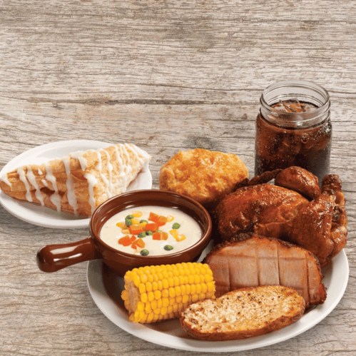 A plate of comfort food featuring fried chicken, corn, mashed potatoes, biscuits, and a dessert, with a drink on the side.