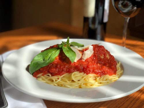 A plate of spaghetti topped with marinara sauce, fresh basil, and cheese, with a glass of red wine in the background.
