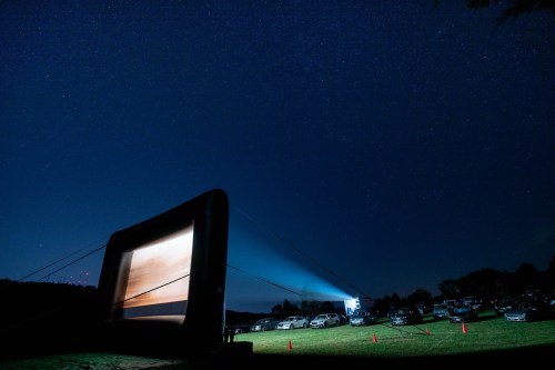An inflatable movie screen set up outdoors at night, with cars parked nearby under a starry sky.