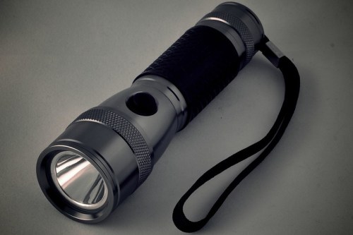 A sleek, metallic flashlight with a textured grip and a wrist strap, resting on a neutral background.