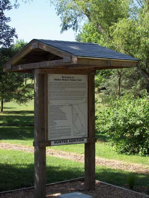 Signpost at Hidden Western Nature Park, featuring a map and welcome information, surrounded by greenery.