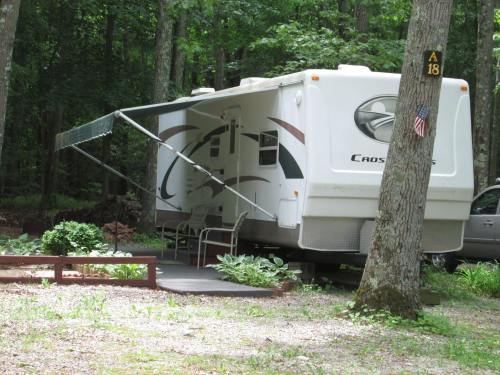 A white RV parked in a wooded area, with an awning extended and a small garden in front.