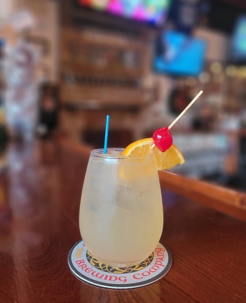 A refreshing cocktail in a glass, garnished with an orange slice and a cherry, on a bar counter.