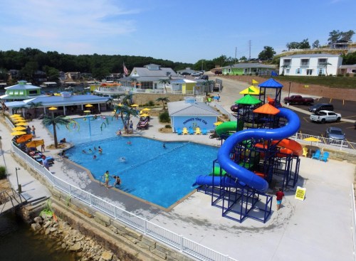 Aerial view of a vibrant pool area with a water slide, palm trees, and people enjoying the water on a sunny day.