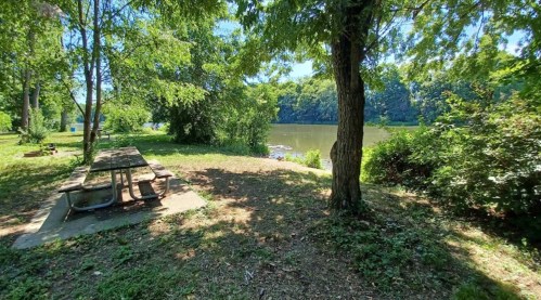 A serene riverside scene featuring a picnic table surrounded by lush greenery and trees.