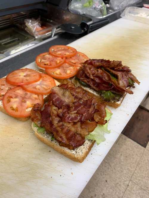 Two slices of bread topped with layers of crispy bacon and fresh tomato slices on a cutting board.