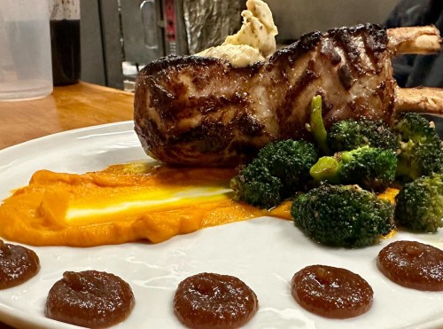 A grilled meat dish with mashed sweet potatoes, broccoli, and sauce drizzles on a white plate.