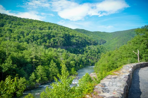 A scenic view of a river winding through lush green mountains under a bright blue sky.