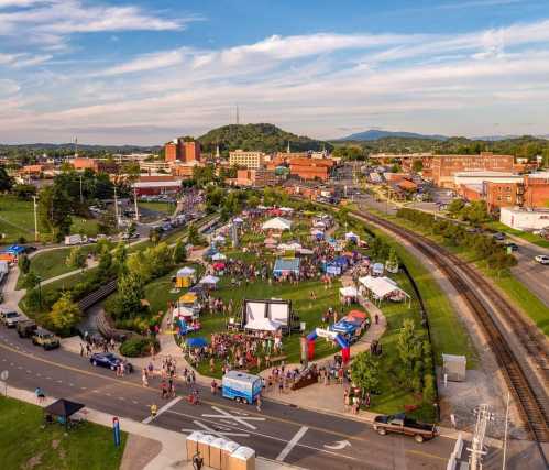 Aerial view of a vibrant outdoor festival with tents, crowds, and a backdrop of hills and buildings.